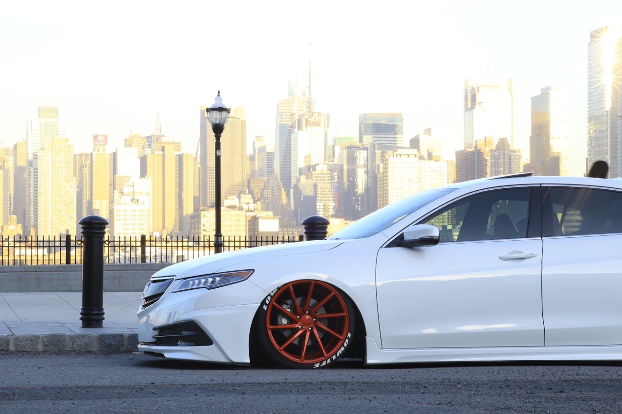 Custom lowered car with vibrant red rims against NYC skyline. Perfect for car enthusiasts.